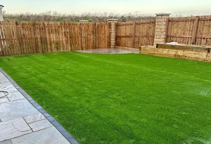 The same garden finished with an artificial lawn, a grey sandstone path and a timber sleeper raised bed