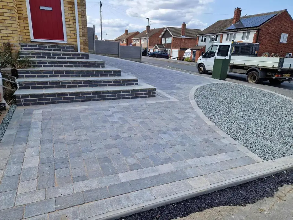 Grey block paved driveway with brick-edged front steps and a curved gravel bed