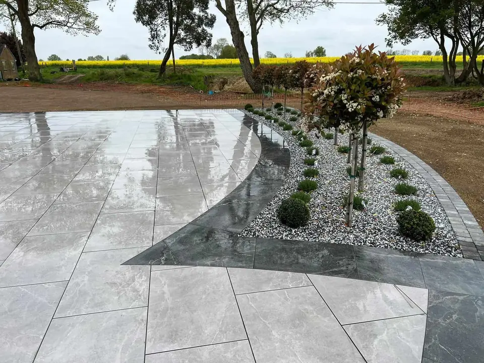 Large light grey porcelain patio with a dark porcelain band and gravel planting beds