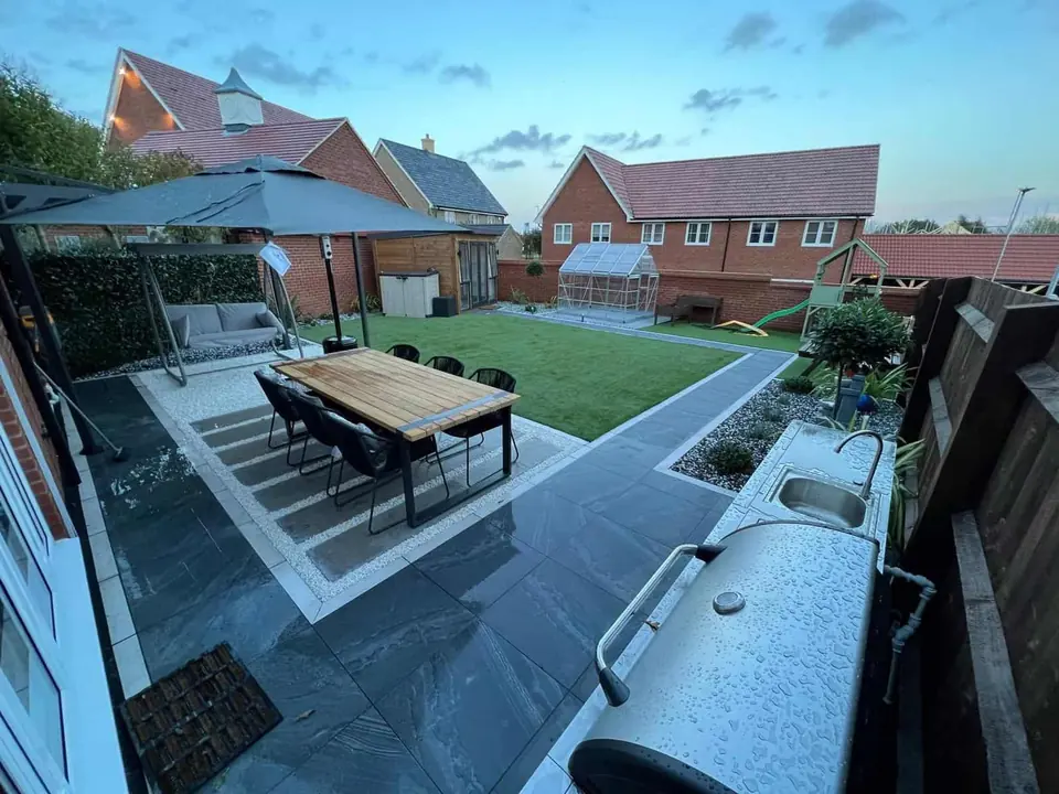 Dark porcelain patio with light paving bands, an outdoor dining table and a lawn beyond