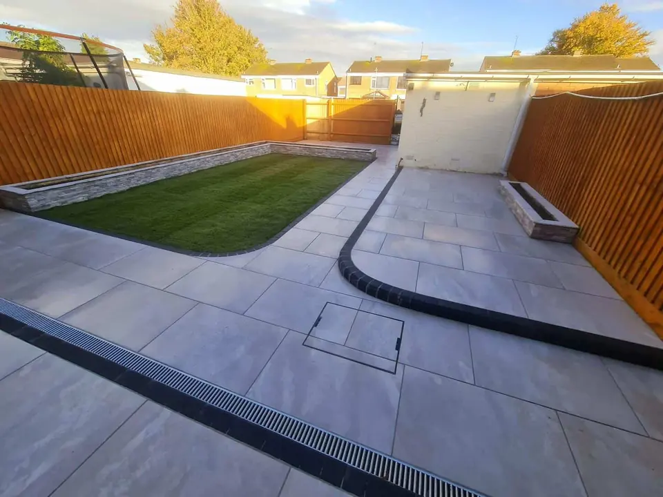 Grey porcelain patio with a linear drainage channel curving around a new lawn between timber fences
