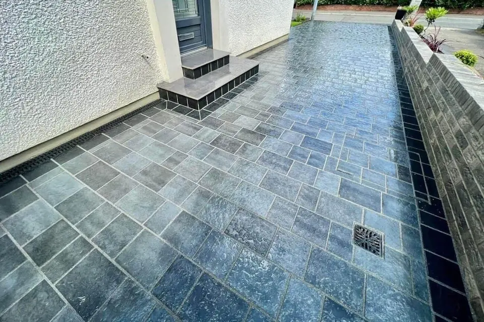 Dark stone paving path running beside a raised planter wall along a rendered house