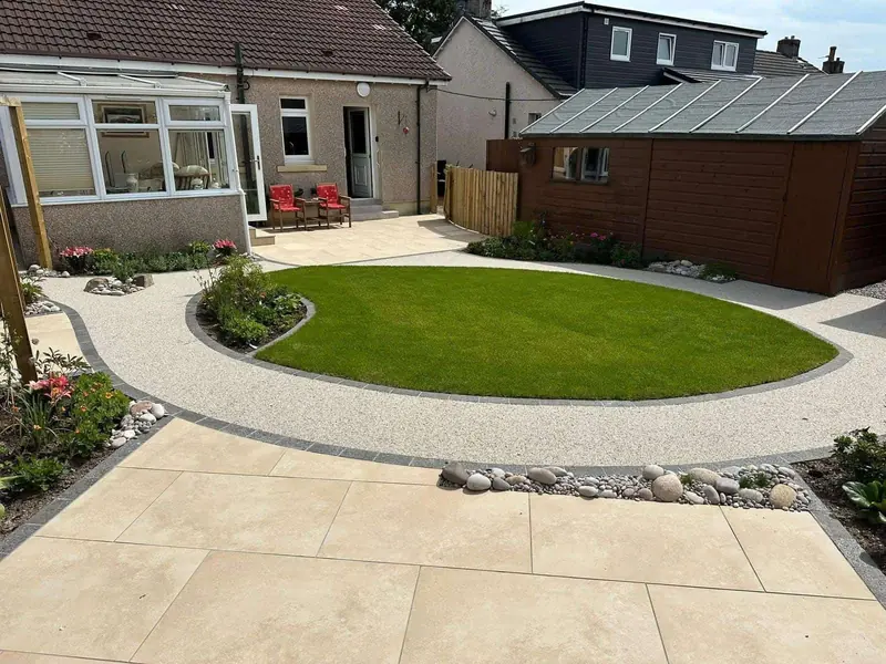 Back garden with a circular lawn, a pale porcelain patio and a curved gravel path edged in dark block